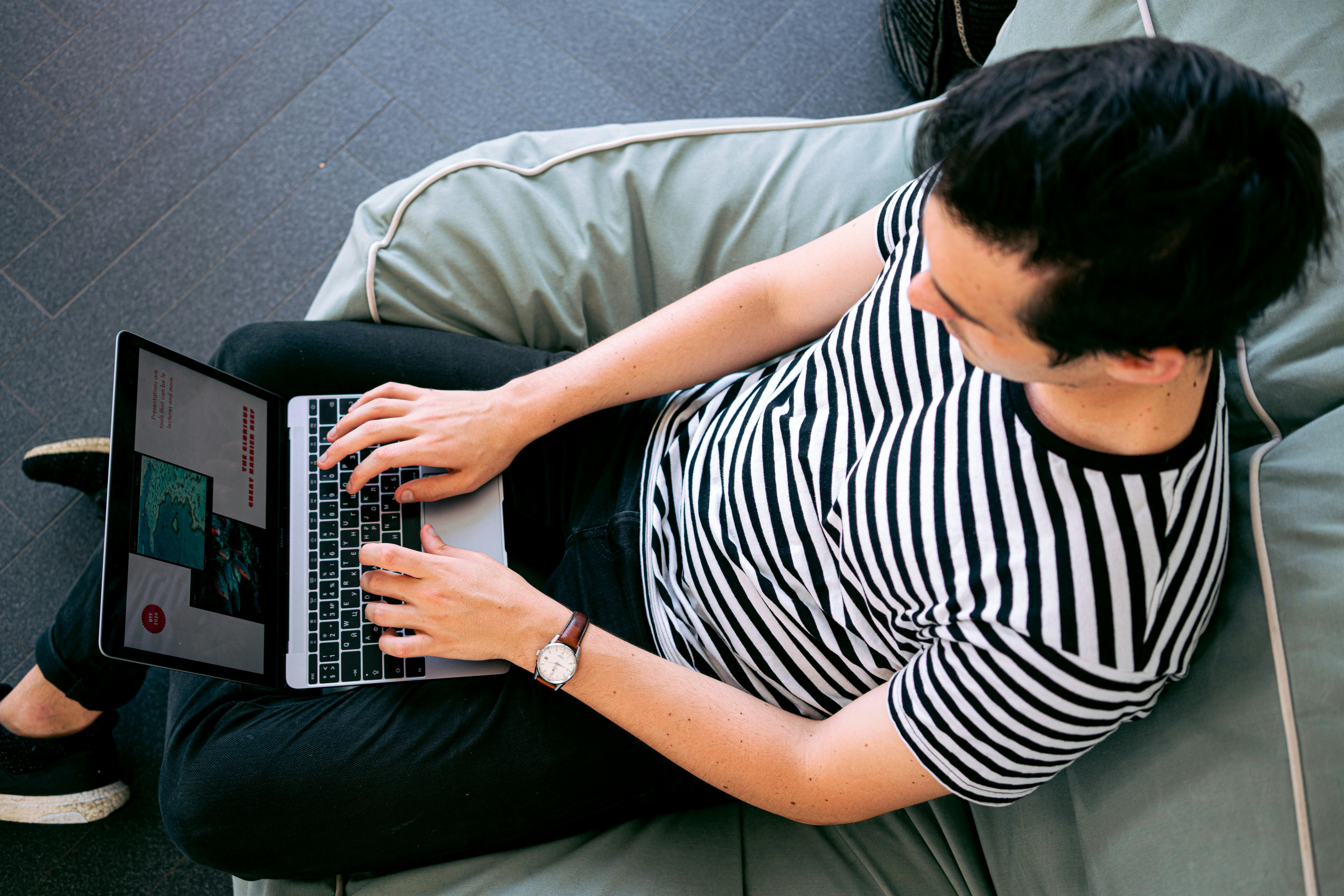 A guy is sitting on a couch and working on a blog content on his laptop